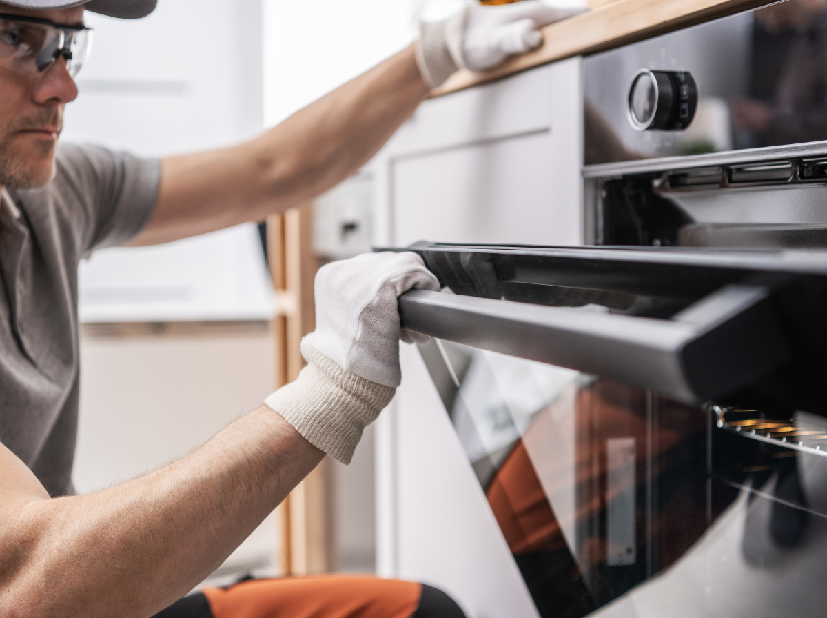 signs oven bake element is bad checking repair Technician wearing safety glasses and white work gloves opening a modern built-in oven door.